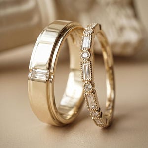 Könnte beinhalten: Ein Paar Goldringe. Der breitere Ring hat einen einzelnen Diamanten im Baguetteschliff, der bündig in die polierte Oberfläche eingelassen ist. Der schmalere Ring ist ein Eternity-Ring mit abwechselnden Baguette- und kleinen Runddiamanten.