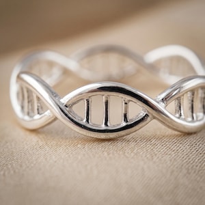 May include: A silver ring featuring a continuous, repeating double helix structure that mimics the shape of a DNA strand. The band is crafted from a polished, reflective metallic material with open spaces between the vertical rungs of the helix.