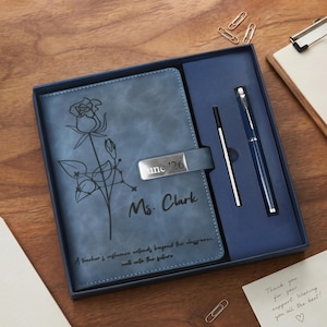 Puede incluir: Un set de cuaderno azul con un dibujo lineal de una rosa, el texto "Ms. Clark" y "June '26", y la cita "A teacher's influence extends beyond the classroom, well into the future." El set incluye un bolígrafo azul a juego y un recambio de tinta negra.