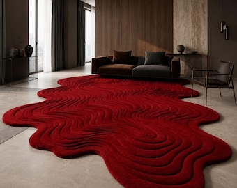 May include: A large, deep red area rug with an irregular, organic shape and a textured, wavy, topographical pattern. The rug features raised, flowing lines that create a sense of depth and movement across its surface, covering a light gray floor.