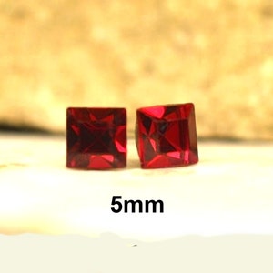 May include: Two red square-shaped gemstones, each measuring 5mm in size. The gemstones are set against a light brown background.