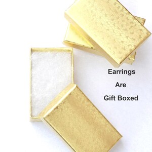 May include: Gold-colored gift boxes, one open to reveal white padding, with the text "Earrings Are Gift Boxed". The boxes have a textured, patterned surface, suggesting a decorative finish.
