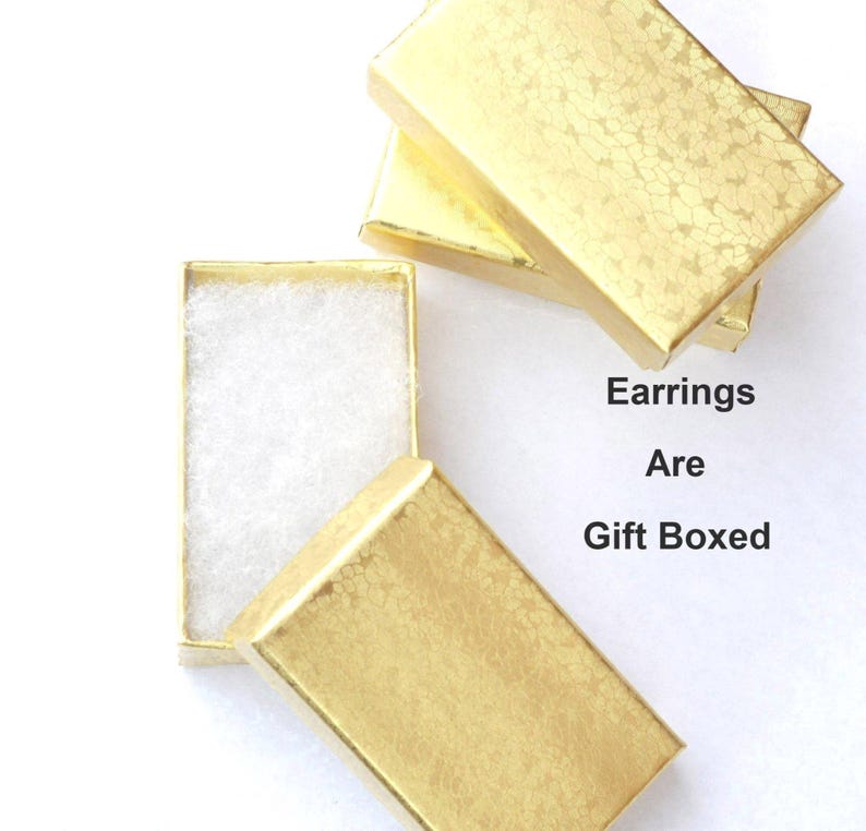 May include: Gold-colored gift boxes, one open to reveal white padding, with the text "Earrings Are Gift Boxed". The boxes have a textured, patterned surface, suggesting a decorative finish.