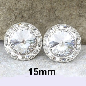 May include: A pair of silver earrings with clear crystal stones, each measuring 15mm in diameter. The stones are surrounded by a silver setting with a decorative border.