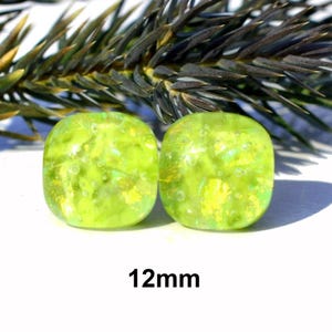 May include: Two square, lime green glass beads with a textured, iridescent finish. The beads are 12mm in size and are displayed against a blurred background of green foliage.