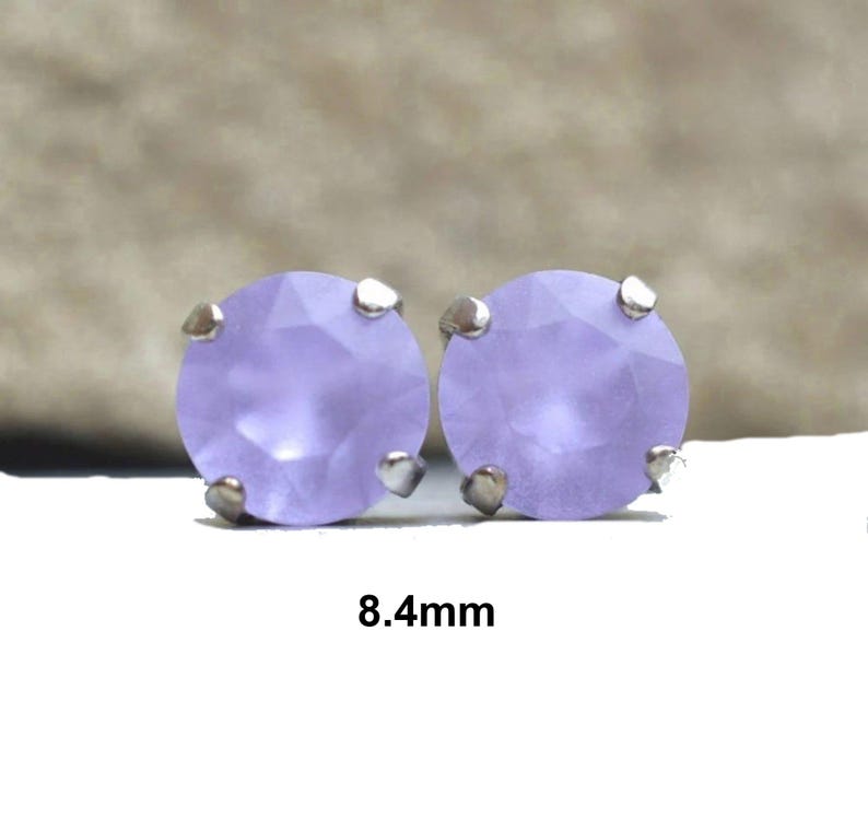 May include: A pair of round, light purple stud earrings. Each earring features a light purple gemstone, approximately 8.4mm in diameter, set in a silver-colored metal. The earrings are displayed on a white surface.