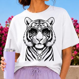 Könnte beinhalten: Ein weißes T-Shirt mit einer schwarz-weißen grafischen Illustration eines Tigers, der eine Sonnenbrille mit Leopardenmuster und eine große, verzierte Halskette im Diamant-Stil trägt. Der Tiger zeigt detaillierte Fellstrukturen und schwarze Streifen.
