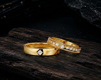 May include: Two gold rings with diamond accents. One ring features a single princess-cut diamond set in a smooth band. The second ring is a band featuring a row of small round diamonds set within a milgrain-detailed channel along the center.