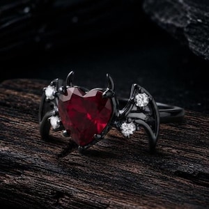 Anillo vintage con forma de corazón y rubí, alas de murciélago y banda de moissanita en oro rodiado negro.