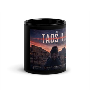 Peut inclure: Un mug en céramique noire avec une impression graphique intitulée The Taos Hum. Le design montre un paysage désertique au coucher du soleil, une personne se couvrant les oreilles, une onde sonore rouge et du texte sur les effets physiques.