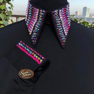 May include: A black long-sleeve shirt featuring a pointed collar and cuffs embellished with rows of multi-colored, iridescent crystals in shades of pink, purple, and blue. The shirt includes a logo patch reading Saddle & Stitched.
