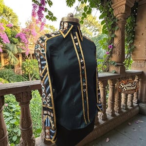 May include: A dark green long-sleeve shirt featuring a structured collar and button-down front. The sleeves and front placket are heavily embellished with gold trim, geometric patterns, and various reflective crystals and metallic accents.