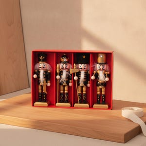 Könnte beinhalten: Ein Set aus vier hölzernen Nussknacker-Figuren in einer roten rechteckigen Schachtel. Jeder Nussknacker trägt eine schwarz-goldene Uniform, einen weißen Kunstfellbart und eine markante Kopfbedeckung wie eine Krone oder Mütze.