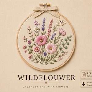 Pode incluir: Um bastidor de bordado circular de madeira contendo um painel de tecido com um arranjo floral costurado à mão de cosmos rosa, lavanda e margaridas brancas. Uma fita bege está amarrada no topo com uma etiqueta marcada BC. Texto: WILDFLOWER.