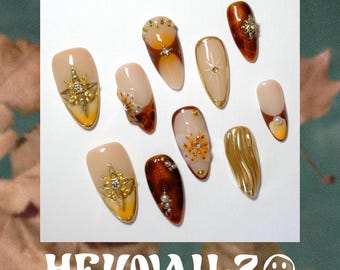 Uñas postizas color ámbar con estampado de carey, set de uñas almendradas de otoño con diseño floral de estrellas doradas.
