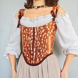 May include: A corset featuring a brown and white deer-inspired spotted fur pattern with dark brown trim and ribbon shoulder ties, worn over a white off-the-shoulder blouse with ruffled sleeves and a plain beige skirt.