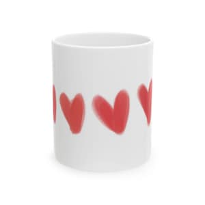 Peut inclure: Mug en céramique blanche orné d'une rangée de cinq cœurs rouges. Les cœurs ont un aspect doux, comme des coups de pinceau, ajoutant une touche artistique au design. Le mug est cylindrique et a une finition lisse et brillante.