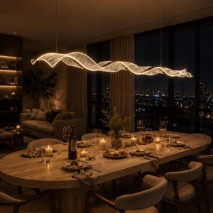 May include: A long, horizontal, wave-shaped LED pendant light fixture with a textured, translucent surface suspended above an oval wooden dining table. The light emits a warm glow, illuminating the table set with plates, glasses, and candles.