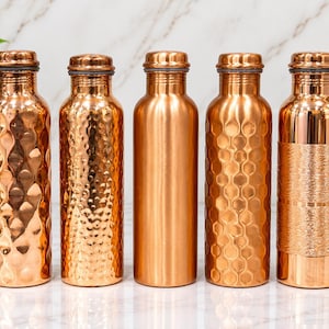 Pode incluir: Cinco garrafas de água cilíndricas de cobre alinhadas. Cada garrafa apresenta uma textura exterior distinta: padrões de ondas verticais, acabamento martelado, superfície lisa polida, design hexagonal de favo de mel e uma faixa gravada.