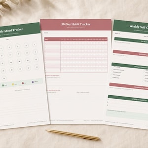 May include: Three open planner pages with green and red accents. The pages include a monthly mood tracker, a 30-day habit tracker, and a weekly self-care check-in. A gold pen rests near the pages.