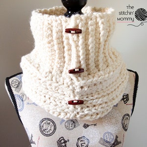 May include: A white crocheted cowl with brown buttons. The cowl is displayed on a mannequin with a patterned fabric background.