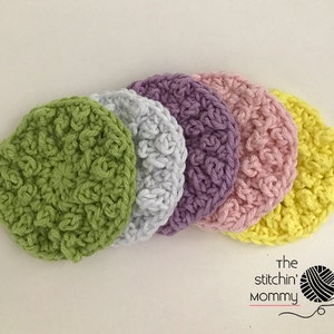 May include: Five crocheted scrubbies in different pastel colors: green, gray, purple, pink, and yellow. The scrubbies are stacked on top of each other.