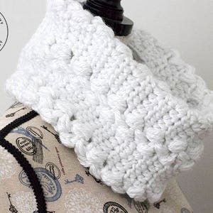 May include: White crocheted infinity scarf with a textured pattern. The scarf is displayed on a mannequin with a floral pattern.