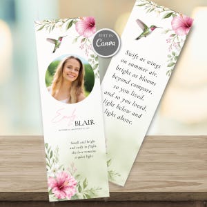 May include: Two vertical memorial bookmarks featuring watercolour pink hibiscus flowers, green foliage, and hummingbirds. One bookmark displays a circular photo of a person, the name Emily Blair, dates, and text. The other features a poem in black serif font.