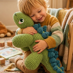 Könnte beinhalten: Ein grünes gehäkeltes Dinosaurier-Spielzeug mit blauen Akzenten wird von einem Kind umarmt. Der Dinosaurier hat große Augen und einen rosa Mund. Das Kind trägt einen gestreiften Pullover und braune Hosen.