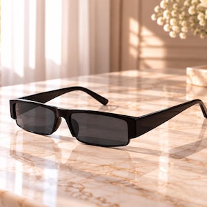 Puede incluir: Gafas de sol rectangulares con montura negra brillante y lentes oscuras. Las gafas presentan una estructura gruesa de plástico de color sólido con patillas rectas y un puente que conecta los dos cristales en un diseño uniforme.