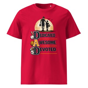 May include: Red t-shirt with a graphic featuring a father and child silhouette walking towards a sunset. The word "DAD" is spelled out with the words "Dedicated, Awesome, Devoted" below, along with sports equipment.