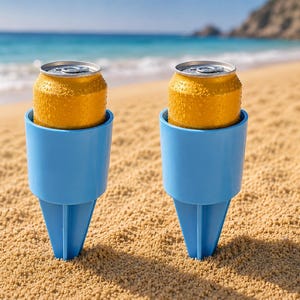 Pode incluir: Dois suportes de bebida de plástico azul-claro com estacas pontiagudas inseridas na areia, cada um contendo uma lata de bebida amarela fria de alumínio com gotas de condensação visíveis na superfície externa das latas.