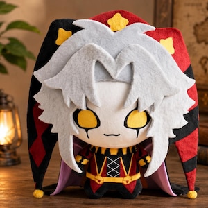 May include: A plush toy featuring a character with spiky light gray hair, large yellow eyes, and black markings under the eyes. The character wears a red and black jester hat with yellow star accents and a matching red, black, and yellow outfit.