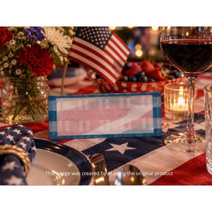 Könnte beinhalten: Eine festliche Tischdekoration mit einer amerikanischen Flagge, Blumen und einer Tischkarte mit rot-weißen Streifen. Ein Glas Rotwein und eine Kerze tragen zur festlichen Atmosphäre bei. Die Tischdecke hat ein Sternmuster.