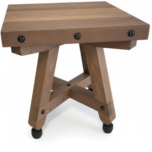 Puede incluir: Una mesa auxiliar cuadrada de madera con acabado de madera natural. La mesa tiene una base en forma de cruz y está asegurada con herrajes de metal negro. La altura de la mesa es de aproximadamente 51 cm.
