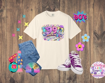 Könnte beinhalten: Ein cremefarbenes Kurzarm-T-Shirt mit einer bunten Grafik und dem Text 1990 MADE IN THE 90s, umgeben von Illustrationen einer Lavalampe, einer Regenbogenspirale, einem digitalen Haustier, einer blauen Jeans und violetten Stoffturnschuhen.