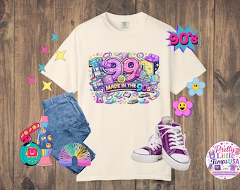 Könnte beinhalten: Ein cremefarbenes T-Shirt mit einer bunten Grafik mit dem Text 1991 und MADE IN THE 90S, umgeben von Illustrationen von Retro-Gegenständen wie einem Kaugummiautomaten, einer Diskette und einer Kassette, kombiniert mit einer blauen Jeans und lila Turnschuhen.