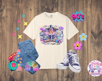 Könnte beinhalten: Ein cremefarbenes T-Shirt mit einem Grafikdruck einer Lavalampe, Kassetten und anderen Retro-Gegenständen mit dem Text "MADE IN THE 90s". Das T-Shirt wird zusammen mit einer blauen Jeans, violetten Turnschuhen und einer Regenbogen-Spirale gezeigt.