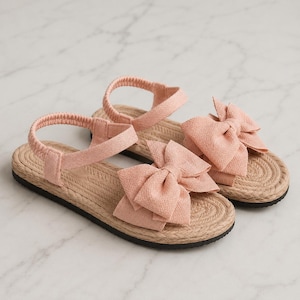 May include: A pair of light pink sandals featuring a large fabric bow on the front strap and an elasticized heel strap. The footbed is constructed with a braided jute-style texture, and the outsole is a solid black rubber material.