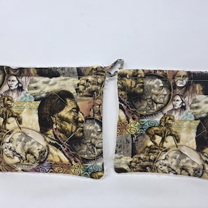 May include: Two square fabric pot holders featuring a collage print of Native American portraits, buffalo, and coin-like circular motifs in shades of brown, tan, and muted earth tones. The quilted items have visible stitching and a small fabric loop.