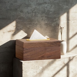Puede incluir: Una caja de pañuelos rectangular de madera marrón oscuro con un acabado de grano liso y un inserto ovalado de color amarillo brillante en la abertura superior, por donde sobresale un pañuelo blanco doblado en forma triangular.