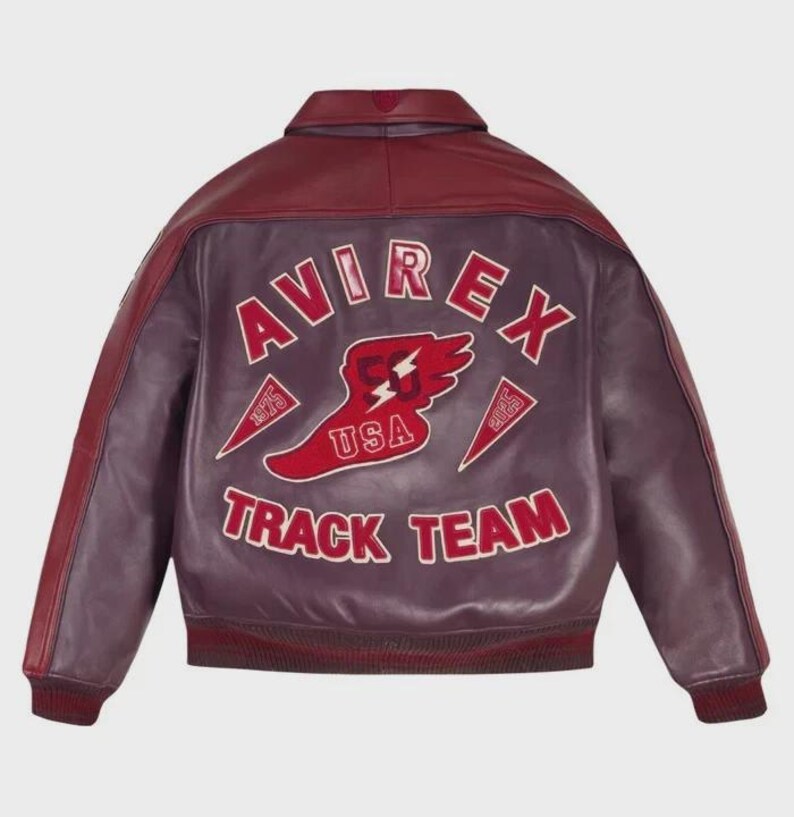 以下が含まれることがあります： 背面にAVIREX TRACK TEAMの赤い文字と白い縁取りの大きなグラフィックが施された、バーガンディ色のレザー製ボンバージャケット。デザインには、USA、1975、2035の文字が入った翼のある足のエンブレムが含まれています。ジャケットには襟、リブ編みの袖口、裾が付いています。