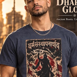 Könnte beinhalten: Ein meliertes marineblaues T-Shirt mit einem zentralen Grafikdruck einer Silhouette, die ein Rad vor einer roten Sonne und dunklen Wolken hält, mit Sanskrit-Text darüber. Das Shirt enthält den Text DHARMIC GLORY und WEAR YOUR HIGHER PURPOSE.