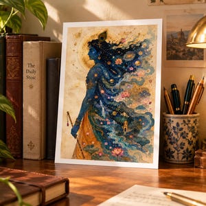 Peut inclure: Une impression d'art rectangulaire représentant le profil d'une divinité à la peau bleue avec une plume de paon dans les cheveux. La silhouette est vêtue d'un vêtement fluide illustrant une scène cosmique avec des planètes, des étoiles et des lotus roses.