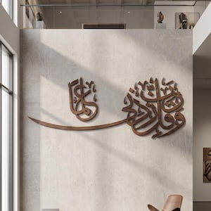 May include: A large, dark brown wooden wall art piece featuring intricate Arabic calligraphy. The design consists of two distinct sections connected by a long, sweeping horizontal stroke, mounted centrally on a light-colored, textured wall.