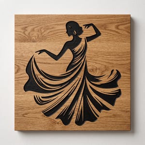 May include: A square wooden wall plaque featuring a black laser-cut or engraved silhouette of a dancer in a flowing dress. The natural light brown wood grain is visible throughout the background, contrasting with the dark, detailed figure.