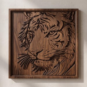 Könnte beinhalten: Ein quadratisches Wandkunstobjekt aus Holz mit einer detaillierten, dreidimensionalen Reliefschnitzerei eines Tigergesichts. Das Kunstwerk ist aus dunkelbraunem Holz mit sichtbarer Maserung gefertigt und zeigt die Augen, Streifen und Schnurrhaare des Tigers.