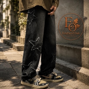 May include: Black denim jeans featuring star-shaped patches. The jeans have a loose fit and are worn with patterned trainers. The EmberrOak Clothing logo is visible in the background.
