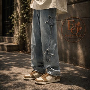 May include: Light blue denim jeans featuring star-shaped cutouts on the knees and thighs. The jeans are worn with brown and cream-coloured trainers. The image is taken outside, with a neutral backdrop.