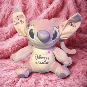 May include: A pink plush toy with large ears, blue eyes, and a grey nose. The ears have the words "I Love You" and "Papa" written on them. The toy's chest has the words "Princess Jazzline" and a pink heart.